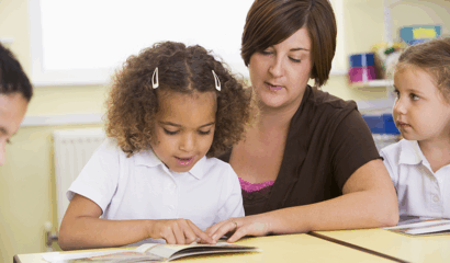 A teacher helps a young girl with reading.